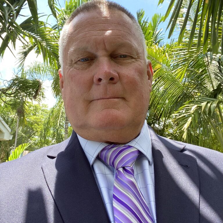 A man in a suit and tie standing under some trees.