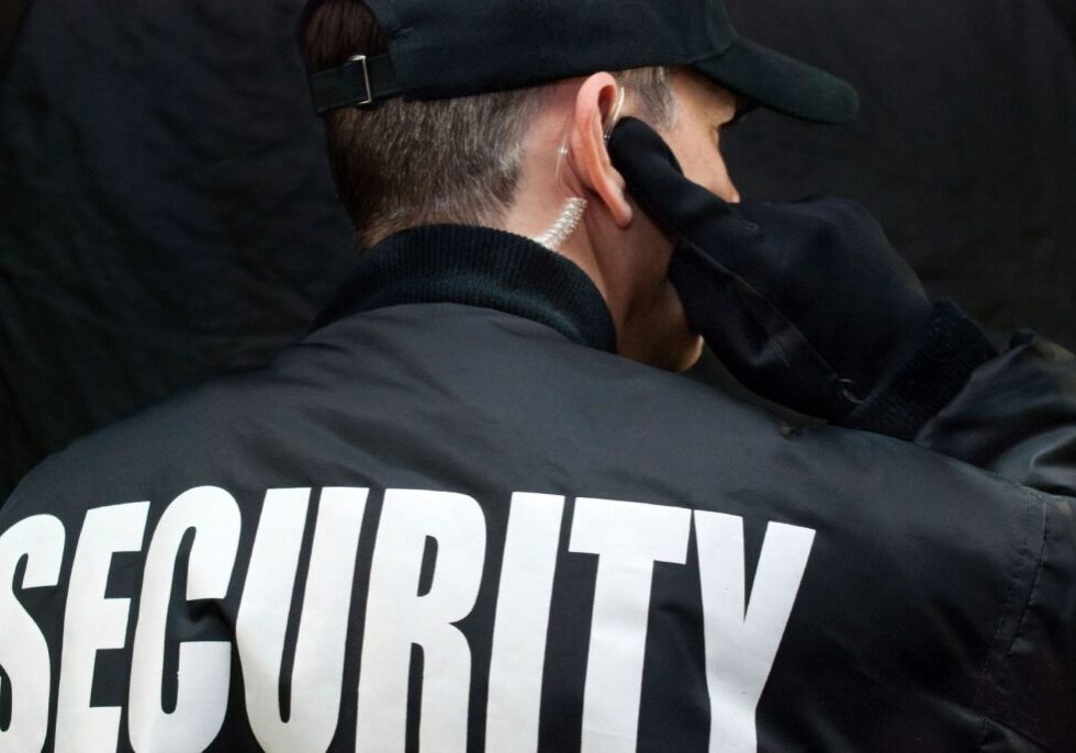 A security guard is wearing his hands behind his head.